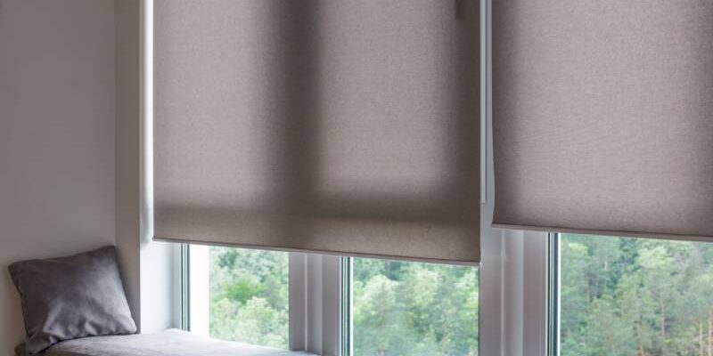 Motorized beige roller shades cover the top half of a window next to a windowsill nook.