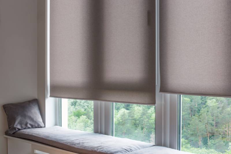 Motorized beige roller shades cover the top half of a window next to a windowsill nook.